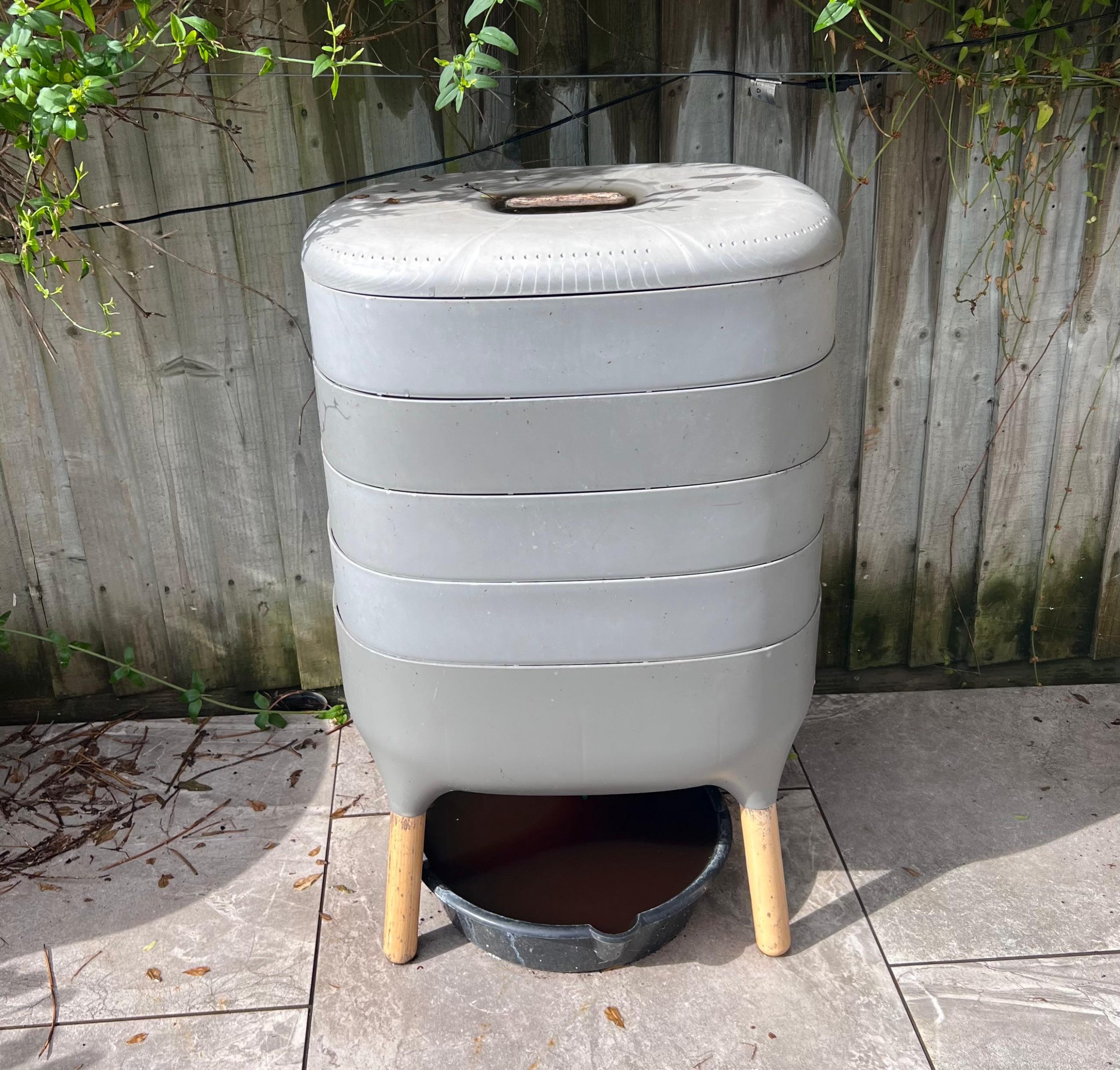 Image shows a wormery with 4 trays against a fence